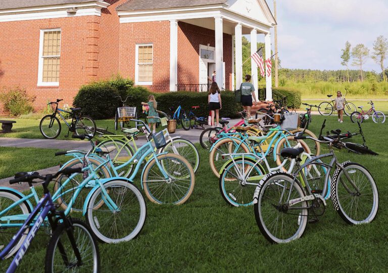 Colorful bicycles parked on a lawn in front of a red brick building with an American flag as children walk toward it.