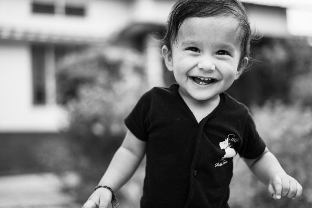 Joyful baby smiling outdoors in a candid black and white shot, capturing a moment of pure happiness.