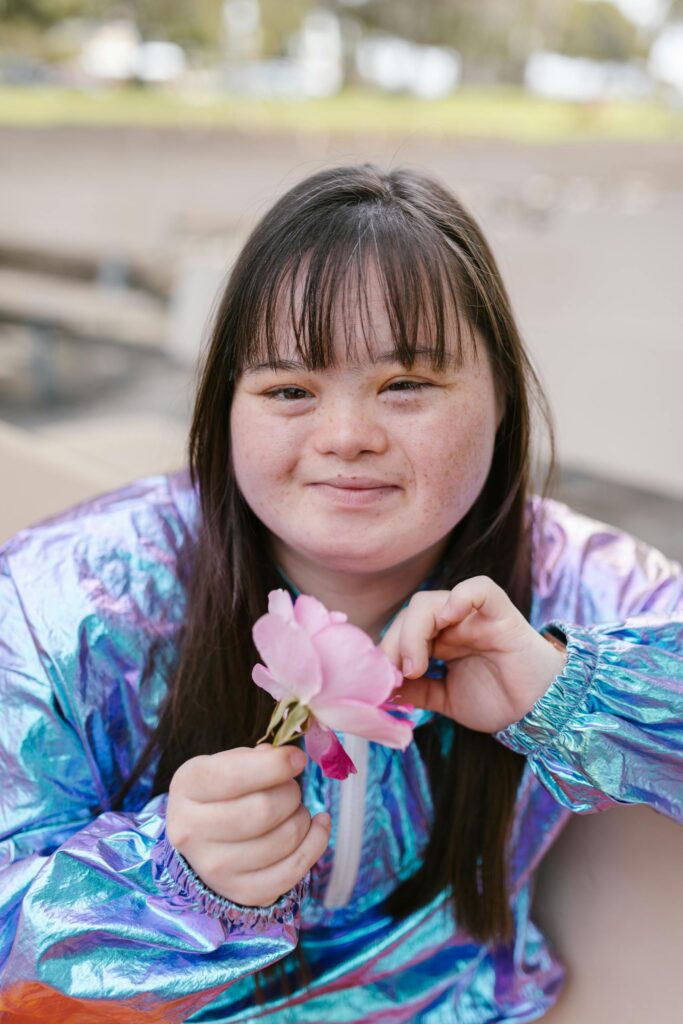 A smiling woman in a reflective jacket holds colorful flowers, enjoying an outdoor day.