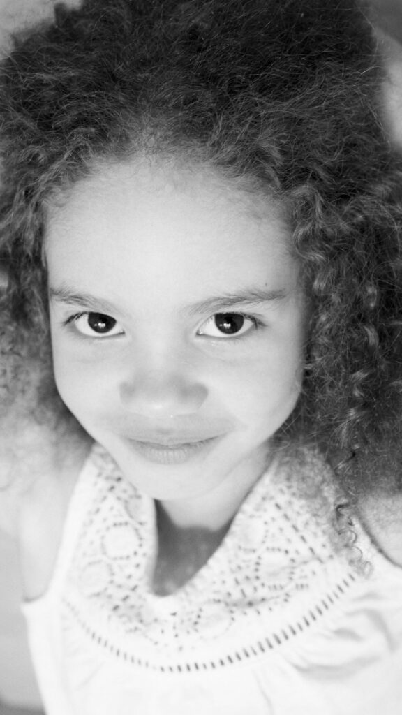A striking black and white portrait of a young girl with curly hair and expressive eyes.