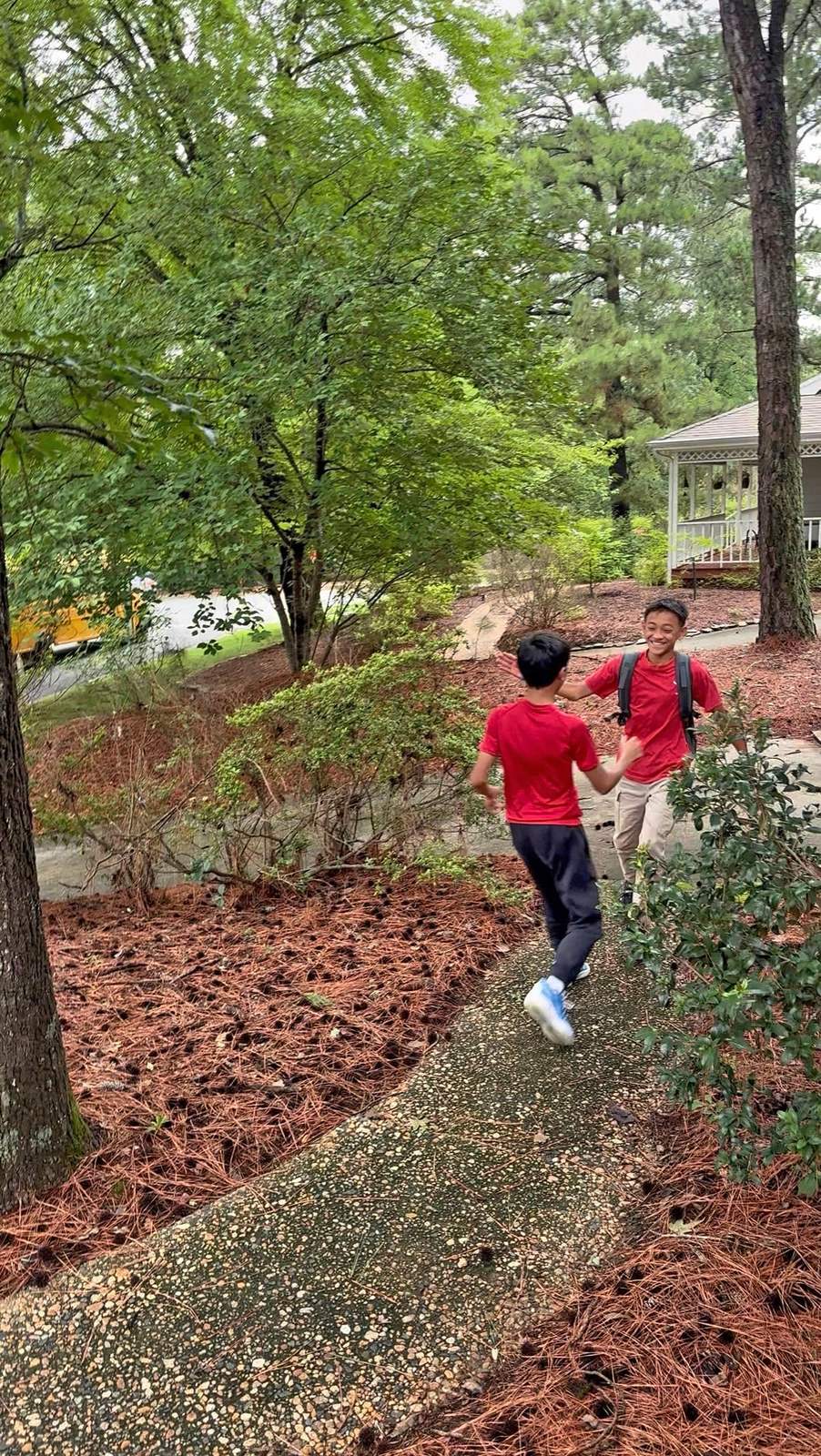 Two boys in red shirts running toward each other on a path, arms outstretched.