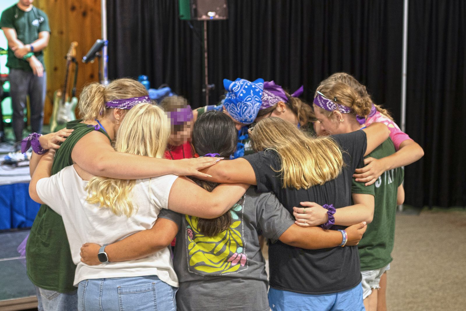 A small group of students huddle together with arms around each other, praying.