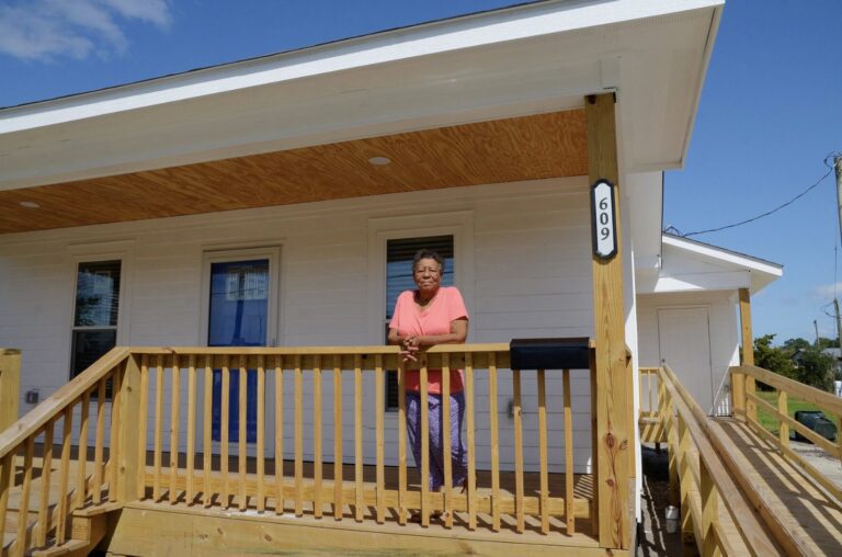 Ina Pickett stands on the porch of her restored home after a call to NCBAM for help.