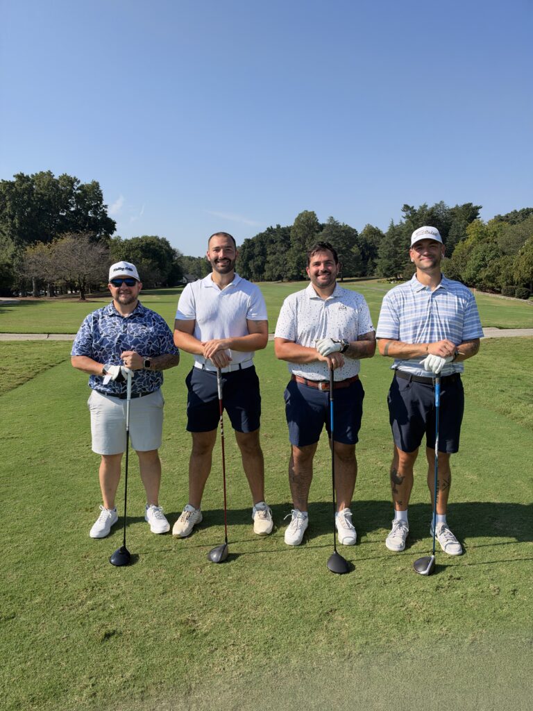 Four men in golf attire pose with clubs on a fairway at the BCH Golf Classic at Sedgefield Country Club.