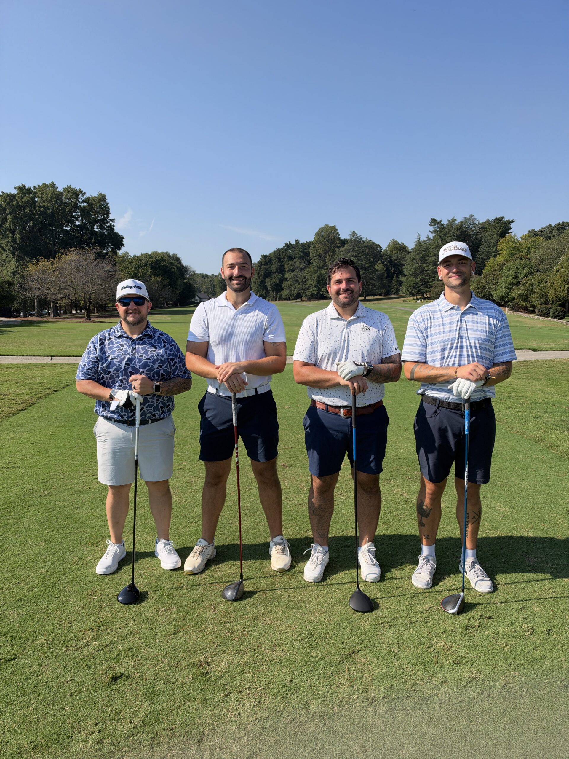 Four men in golf attire pose with clubs on a fairway at the BCH Golf Classic at Sedgefield Country Club.