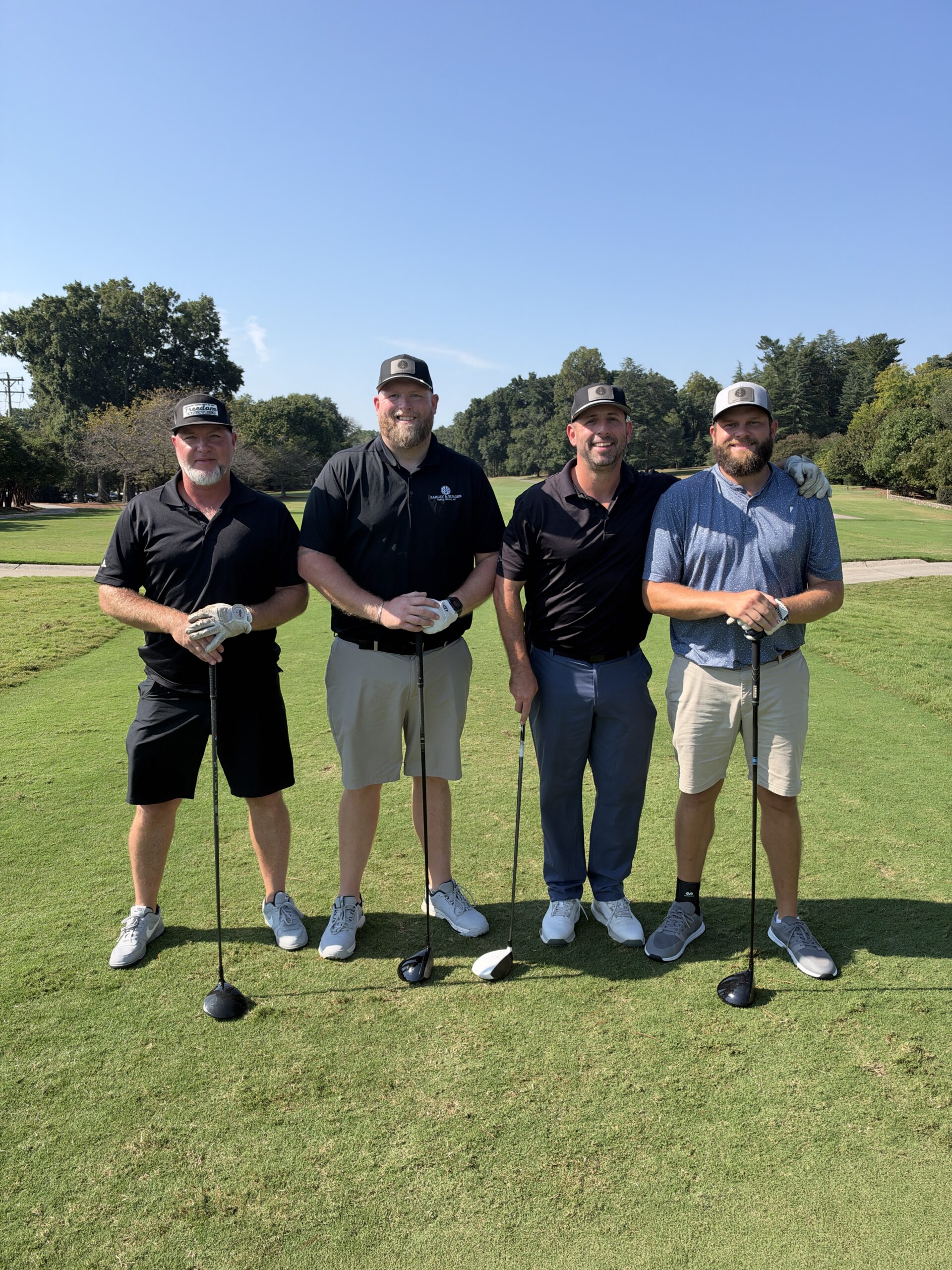 Four men in golf attire pose with clubs on the fairway at the BCH Golf Classic at Sedgefield Country Club.