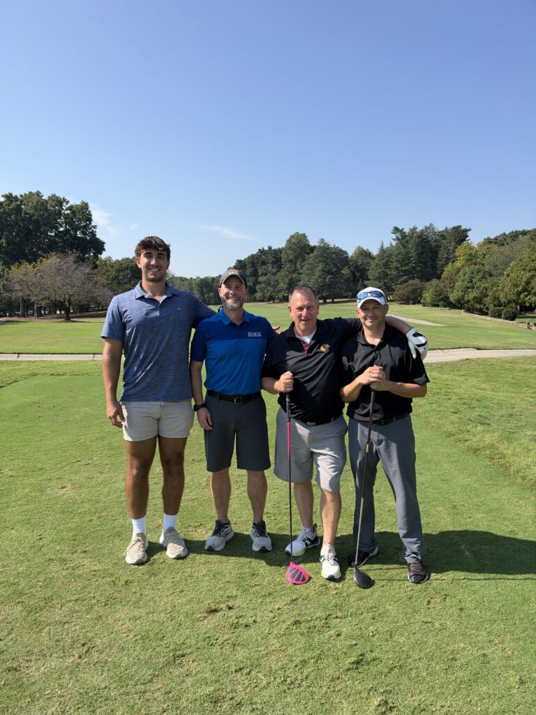 Four men pose together on a sunny golf course at the BCH Golf Classic fundraiser at Sedgefield Country Club.
