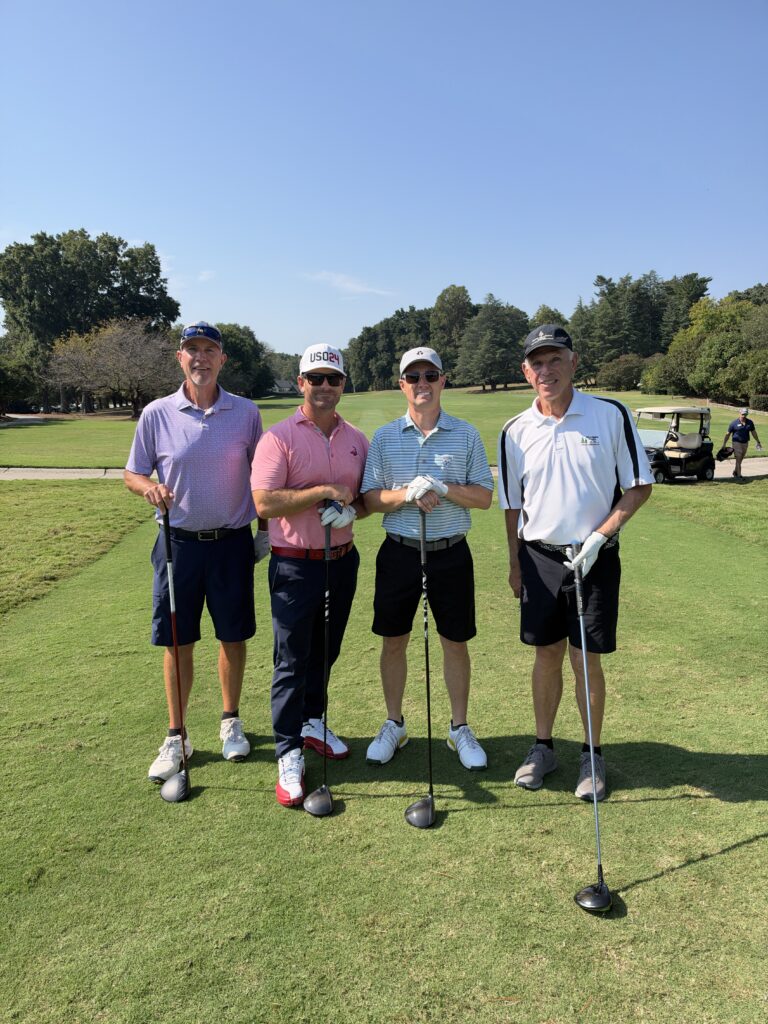 Four men pose with golf clubs on the fairway at the BCH Golf Classic at Sedgefield Country Club on a sunny day.