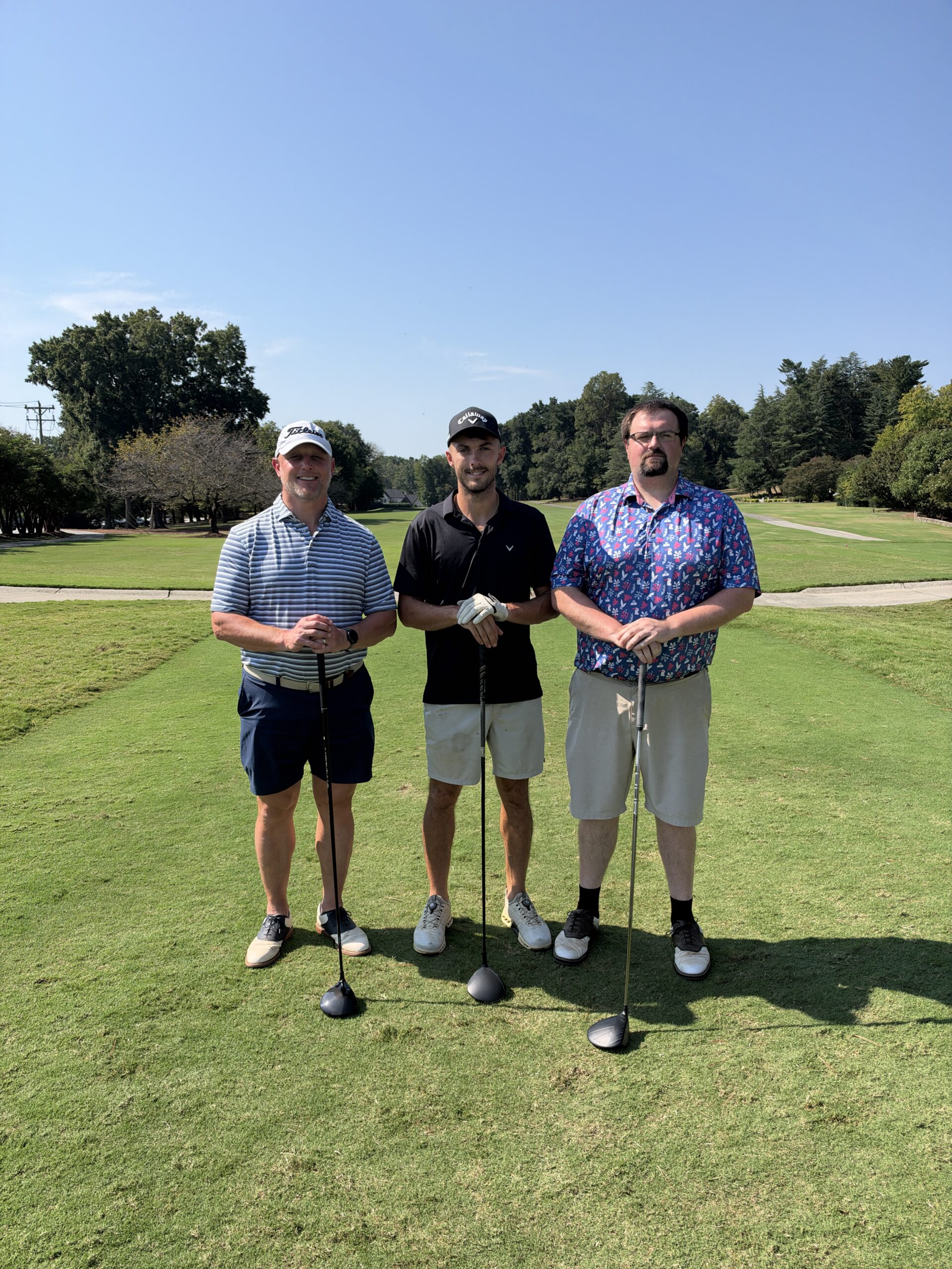 Three golfers pose with drivers on a sunny fairway at the BCH Golf Classic at Sedgefield Country Club.