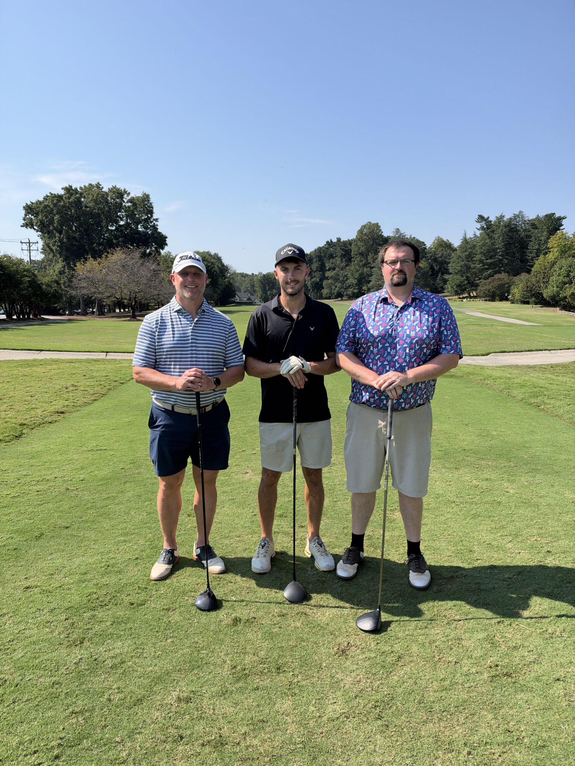 Three men pose with golf clubs on a sunny fairway during the BCH Golf Classic at Sedgefield Country Club.