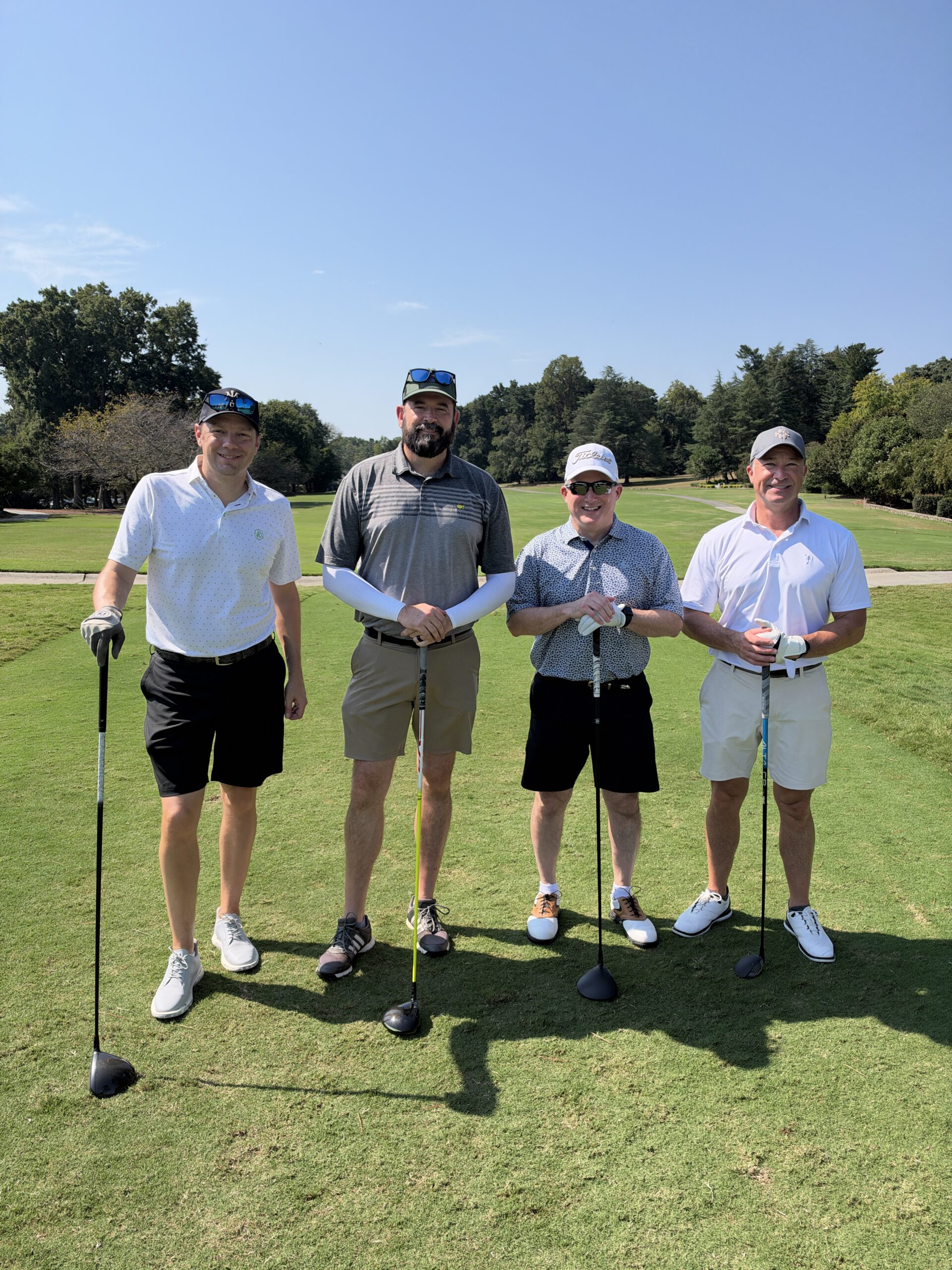 Four men in golf attire pose with clubs on a sunny fairway at the BCH Golf Classic at Sedgefield Country Club.