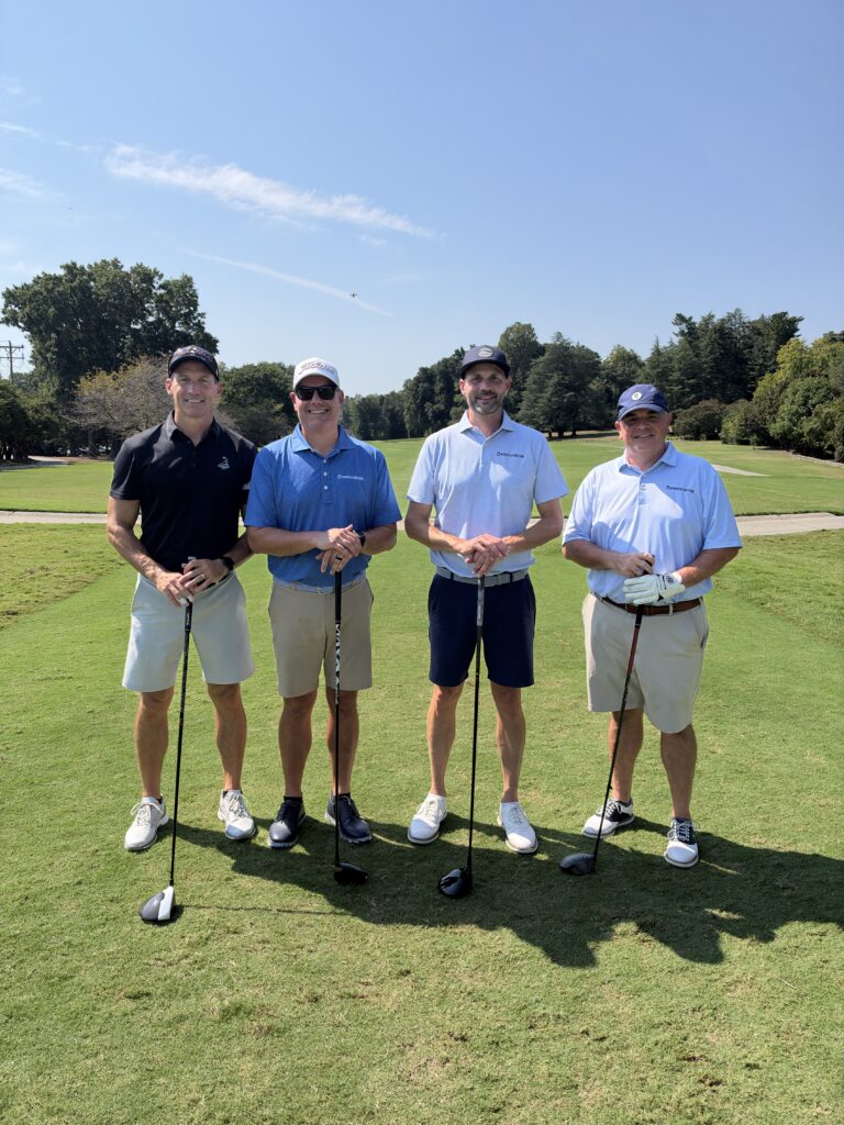 Four men in golf attire pose with clubs on a sunny fairway at the BCH Golf Classic at Sedgefield Country Club.