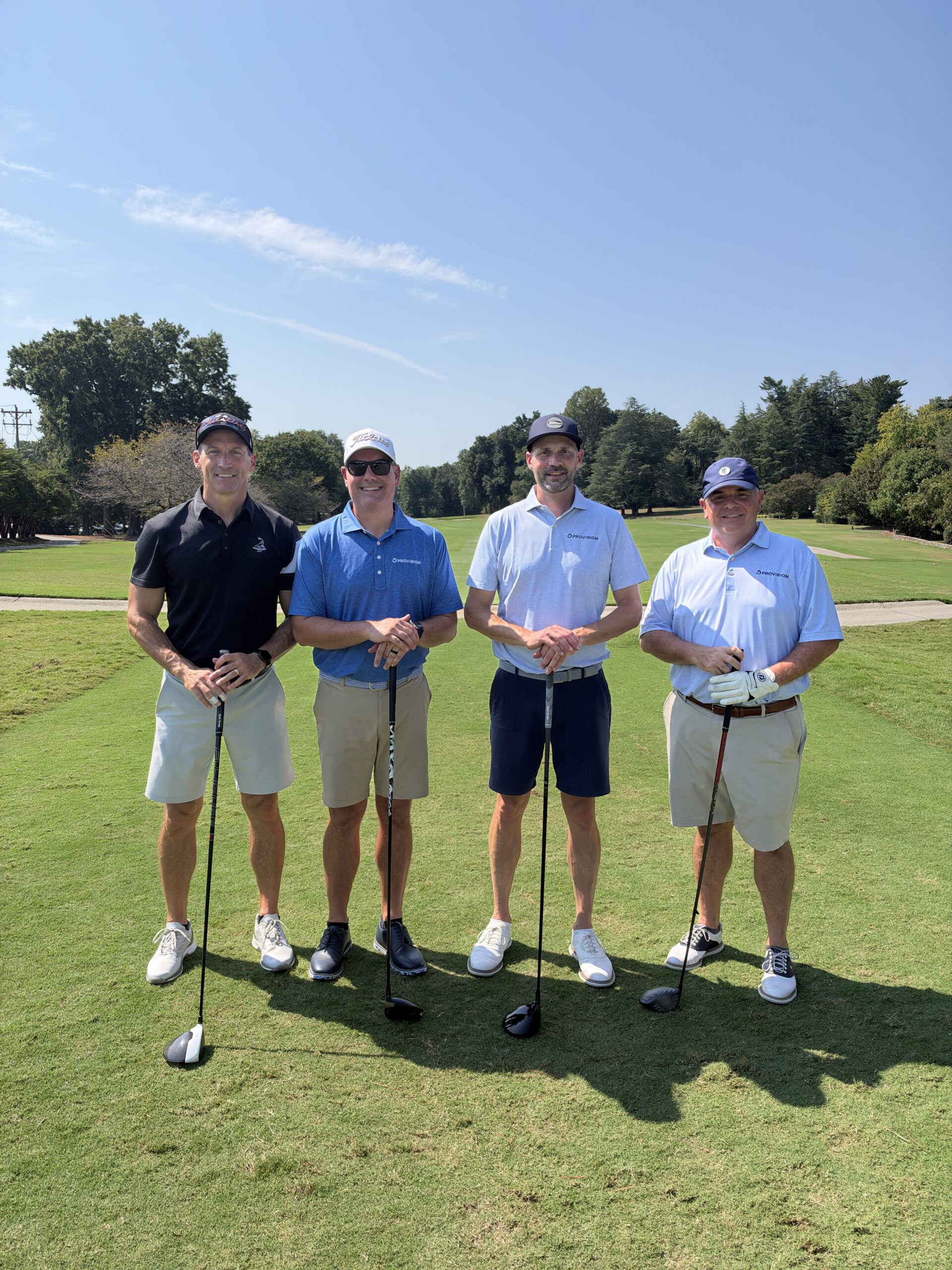 Four men in golf attire pose with clubs on a sunny fairway at the BCH Golf Classic at Sedgefield Country Club.
