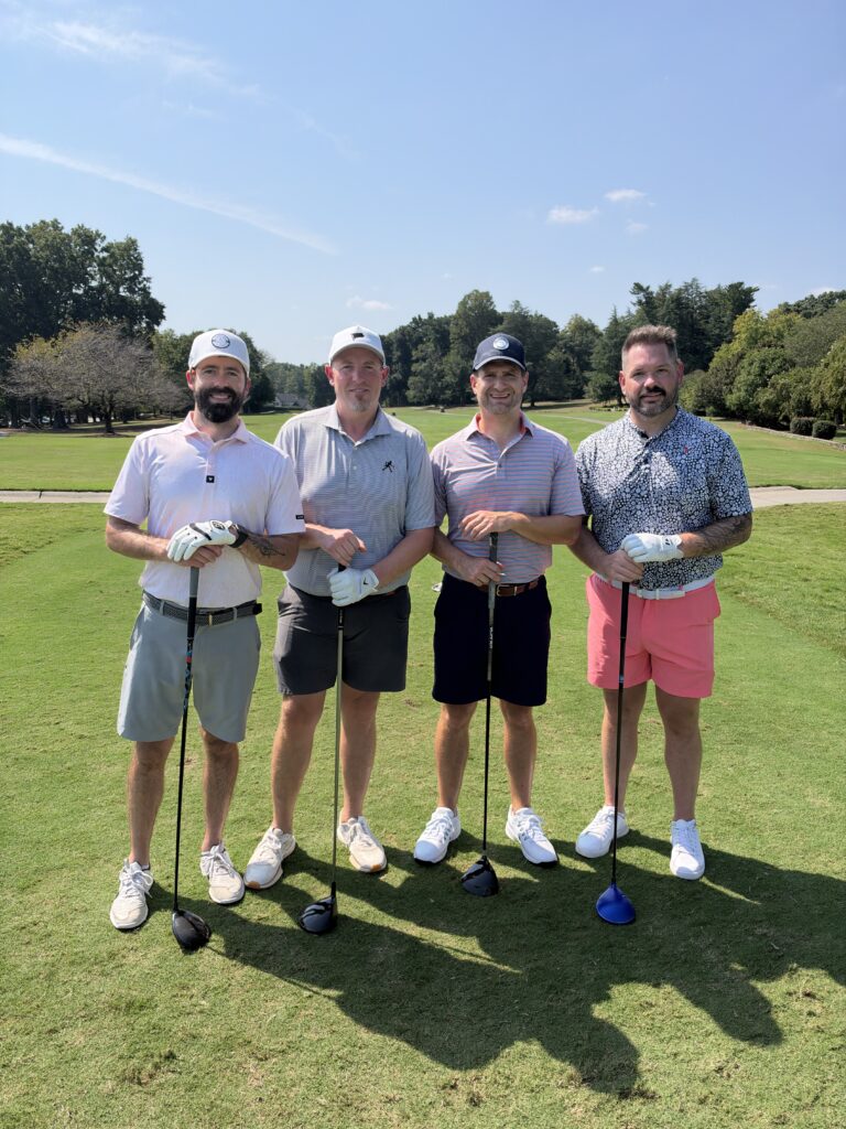 Four men pose with golf clubs on a sunny fairway during the BCH Golf Classic fundraiser at Sedgefield Country Club.