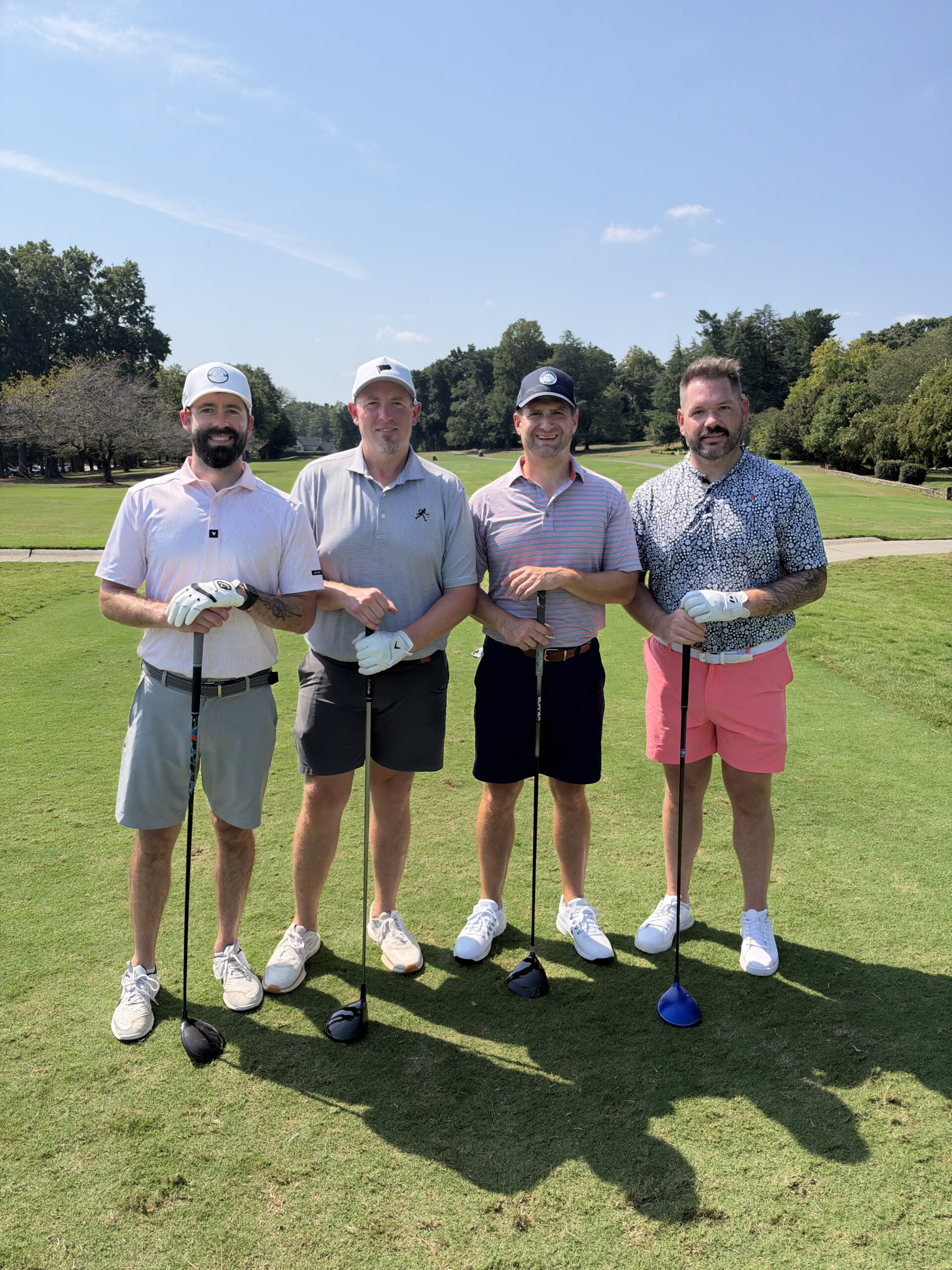 Four men in golf attire pose with clubs on a sunny fairway at the BCH Golf Classic at Sedgefield Country Club.
