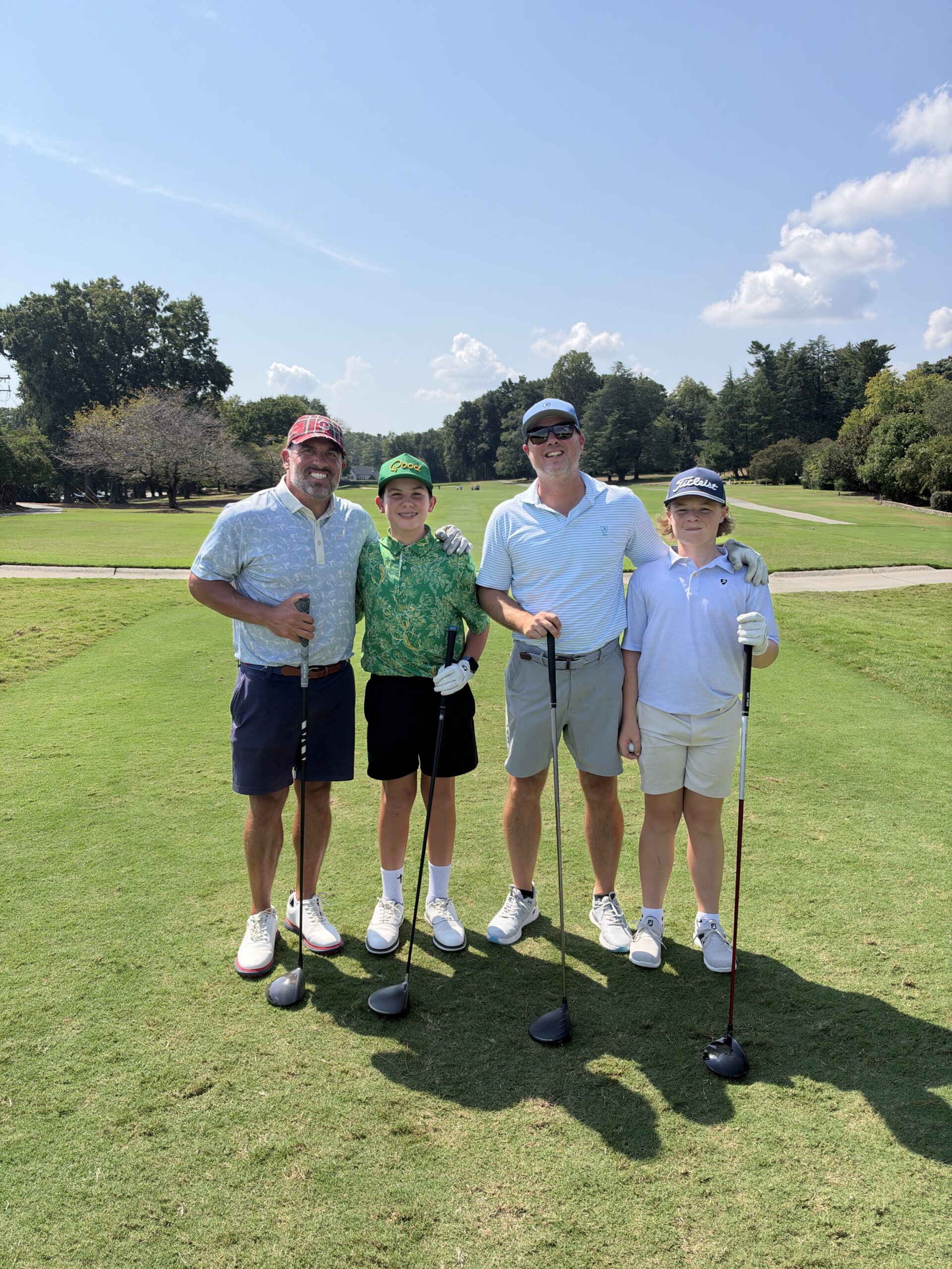 Two men and two boys pose with golf clubs on a fairway at the BCH Golf Classic at Sedgefield Country Club.