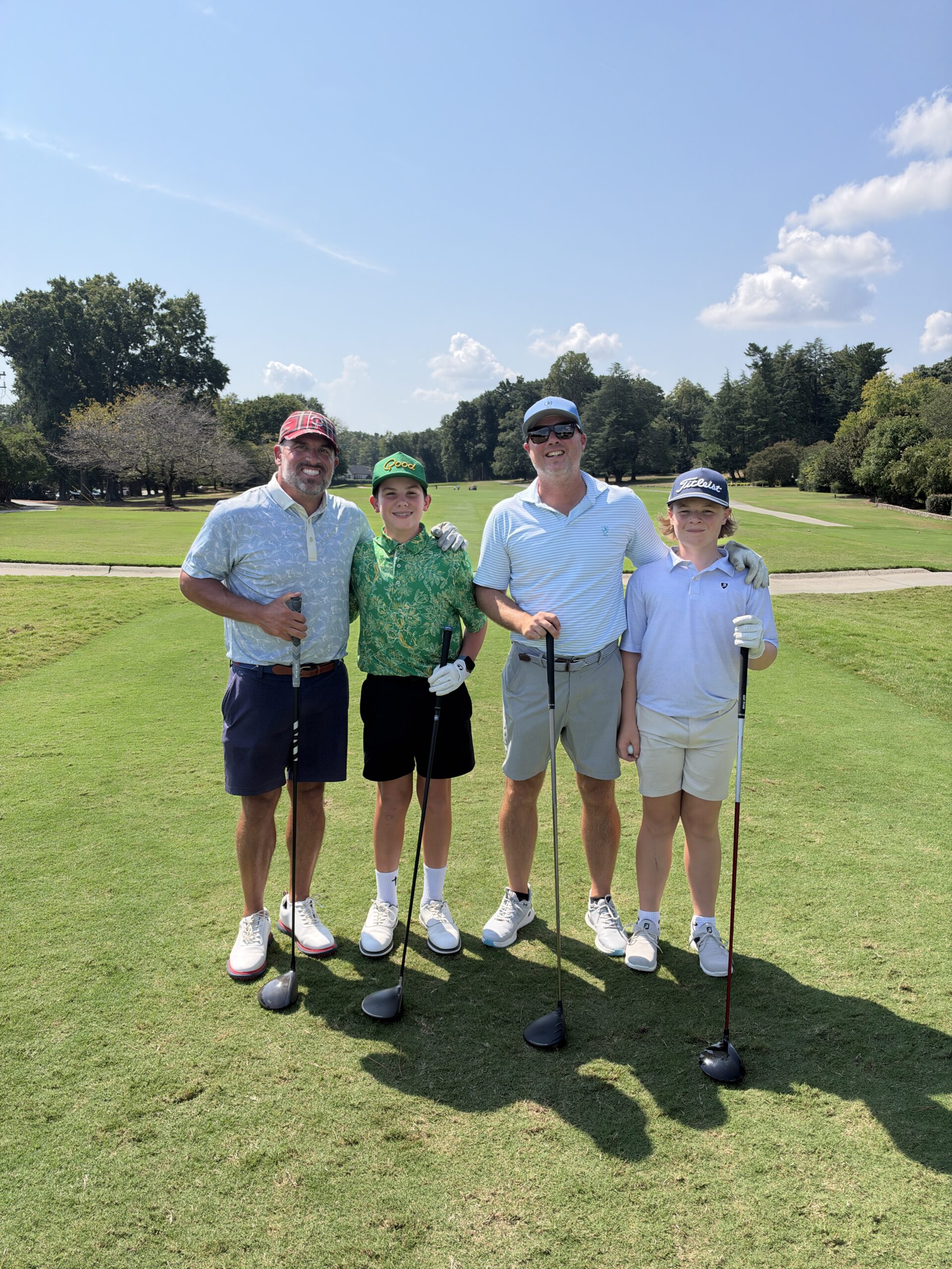 Two men and two boys pose with golf clubs on a sunny fairway at the BCH Golf Classic at Sedgefield Country Club.
