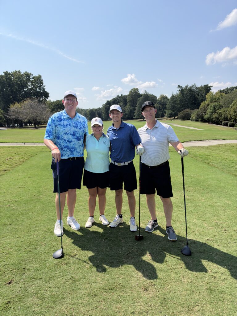 Four golfers pose arm in arm on a sunny fairway at the BCH Golf Classic at Sedgefield Country Club.