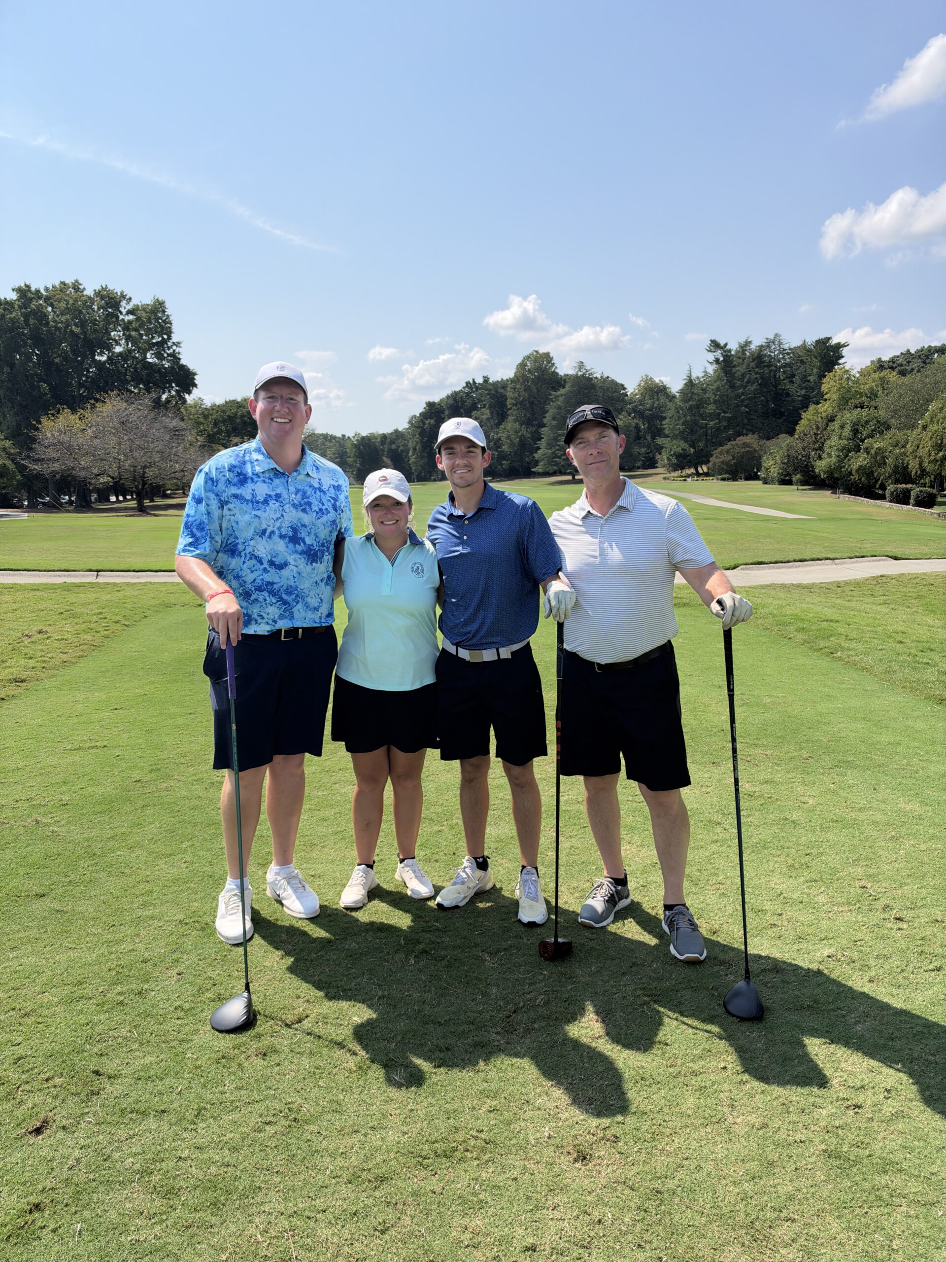 Four golfers pose arm in arm on a sunny fairway at the BCH Golf Classic at Sedgefield Country Club.