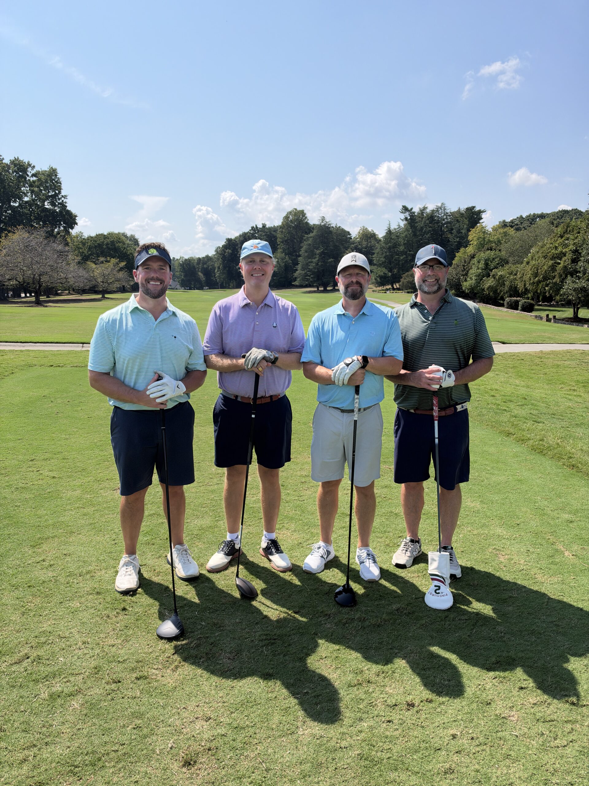 Four men pose with golf clubs on a sunny fairway at the BCH Golf Classic fundraising tournament at Sedgefield Country Club.