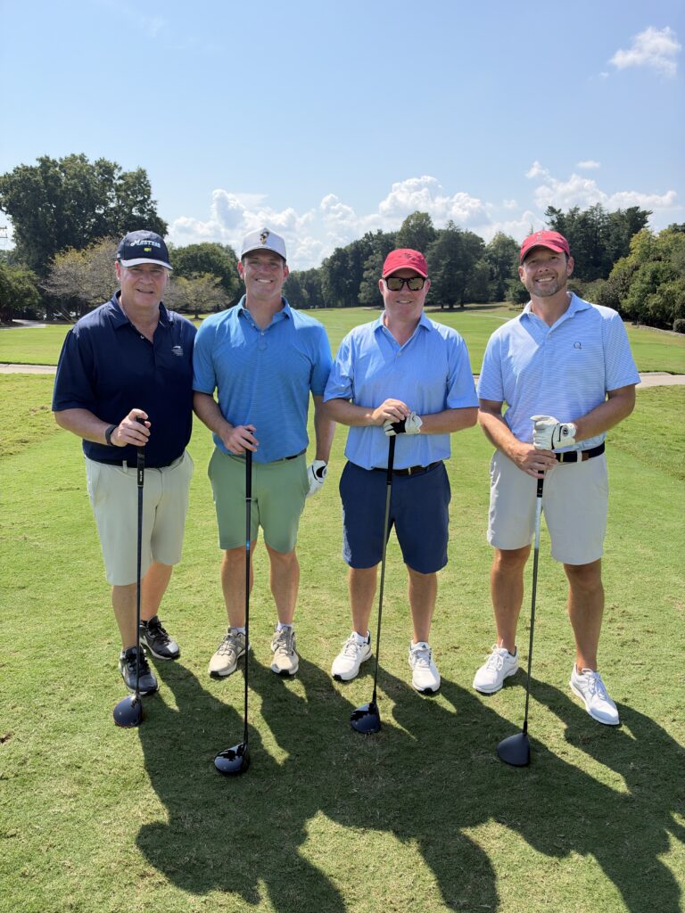 Four men in golf attire pose with drivers on a sunny fairway at the BCH Golf Classic at Sedgefield Country Club.