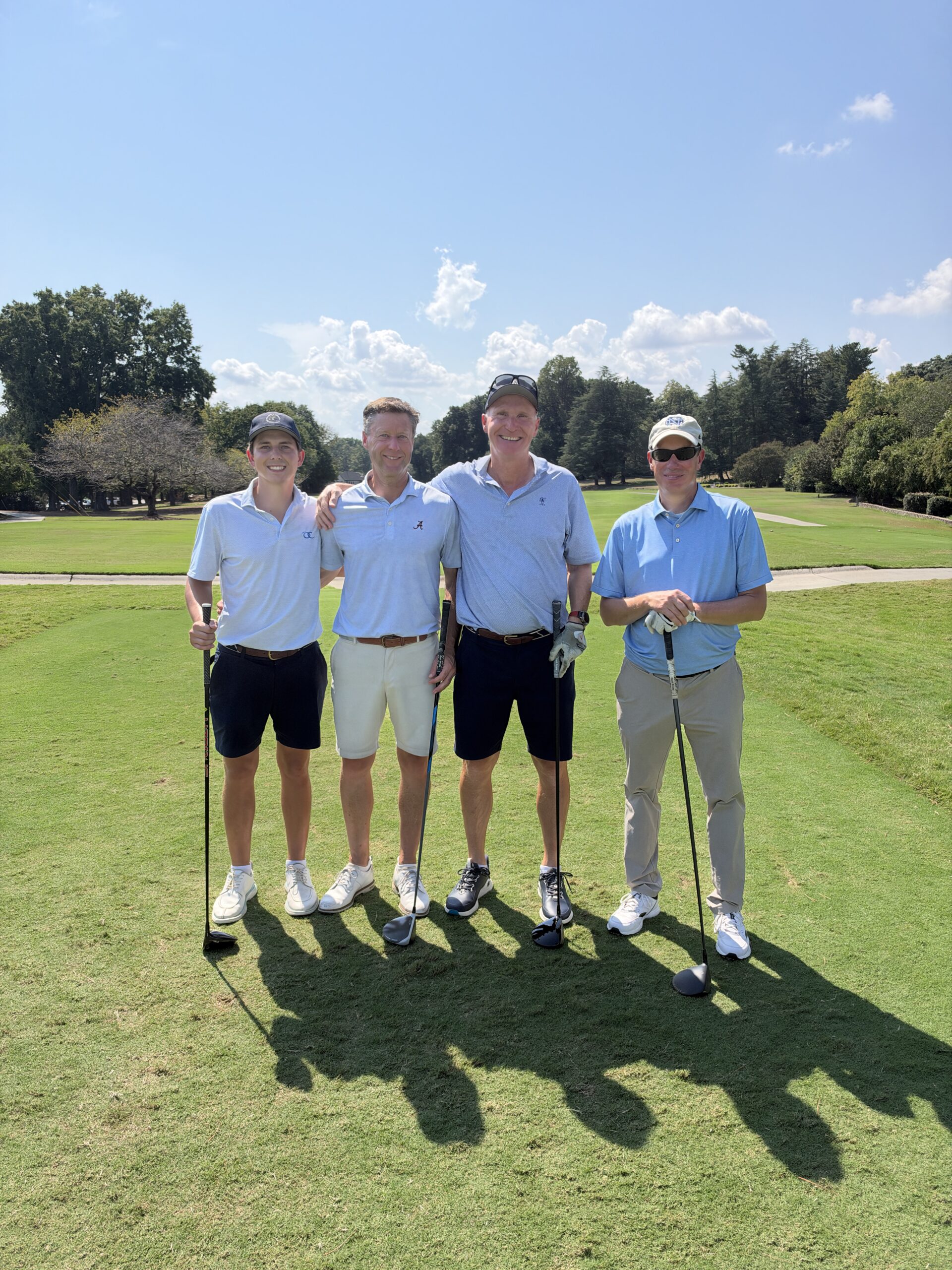 Four men in golf attire pose with clubs on the course at the BCH Golf Classic at Sedgefield Country Club.