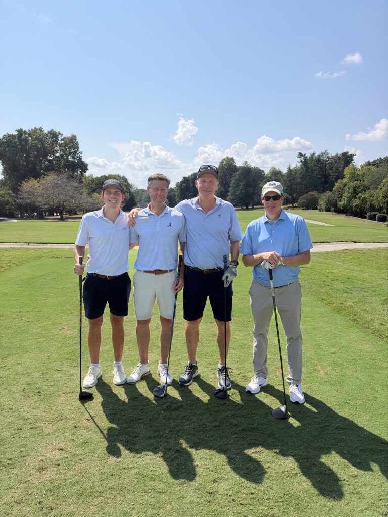 Four golfers in light blue shirts pose together on the course at the BCH Golf Classic at Sedgefield Country Club.