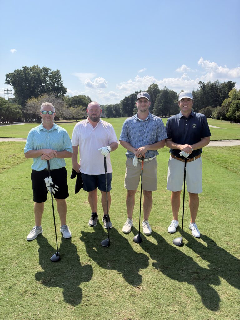 Four men pose with golf clubs on a sunny fairway at the BCH Golf Classic fundraiser at Sedgefield Country Club.