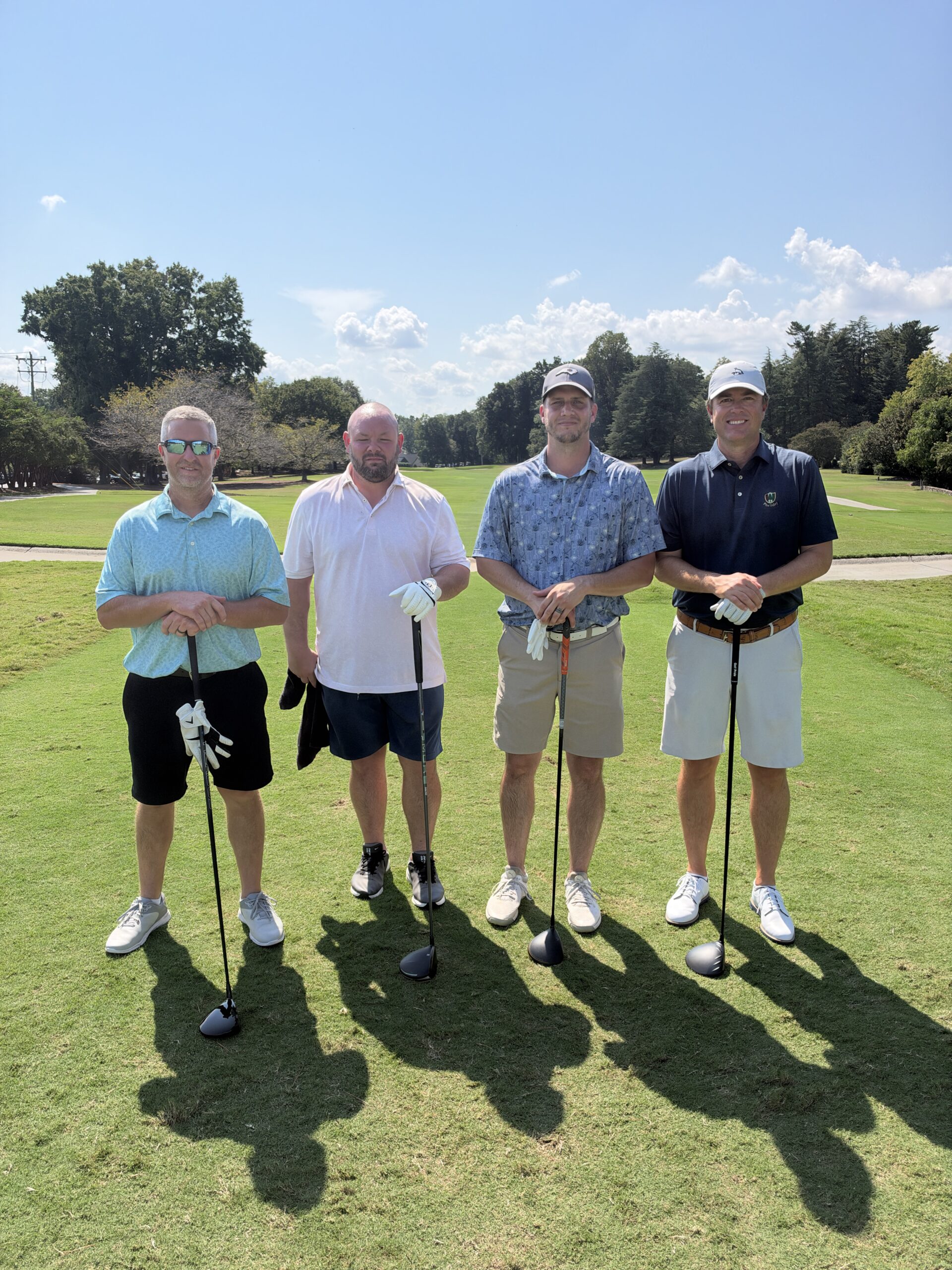 Four men pose with golf clubs on a sunny fairway at the BCH Golf Classic fundraiser at Sedgefield Country Club.