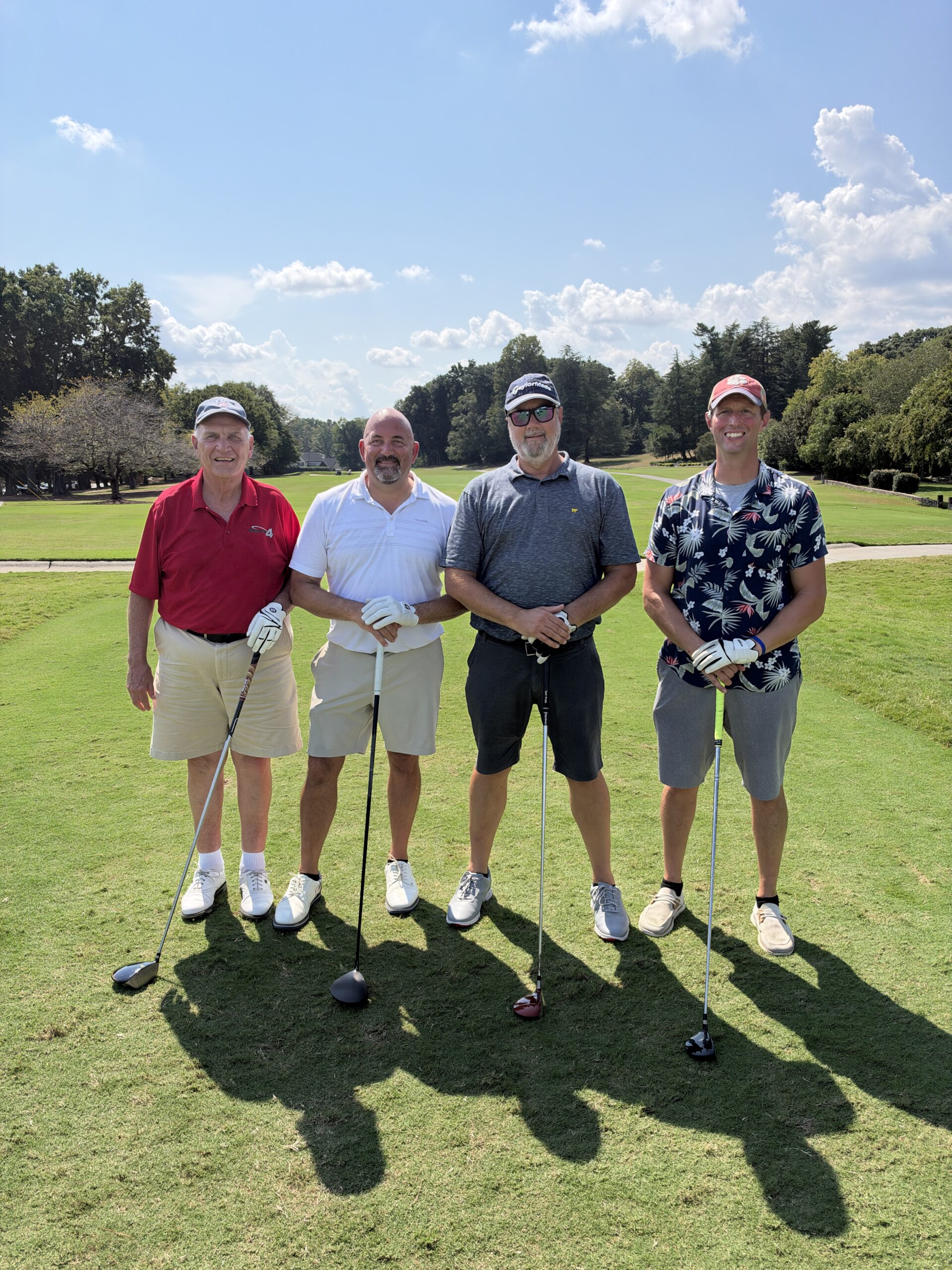 Four men pose with golf clubs on a sunny fairway at the BCH Golf Classic fundraising tournament at Sedgefield Country Club.