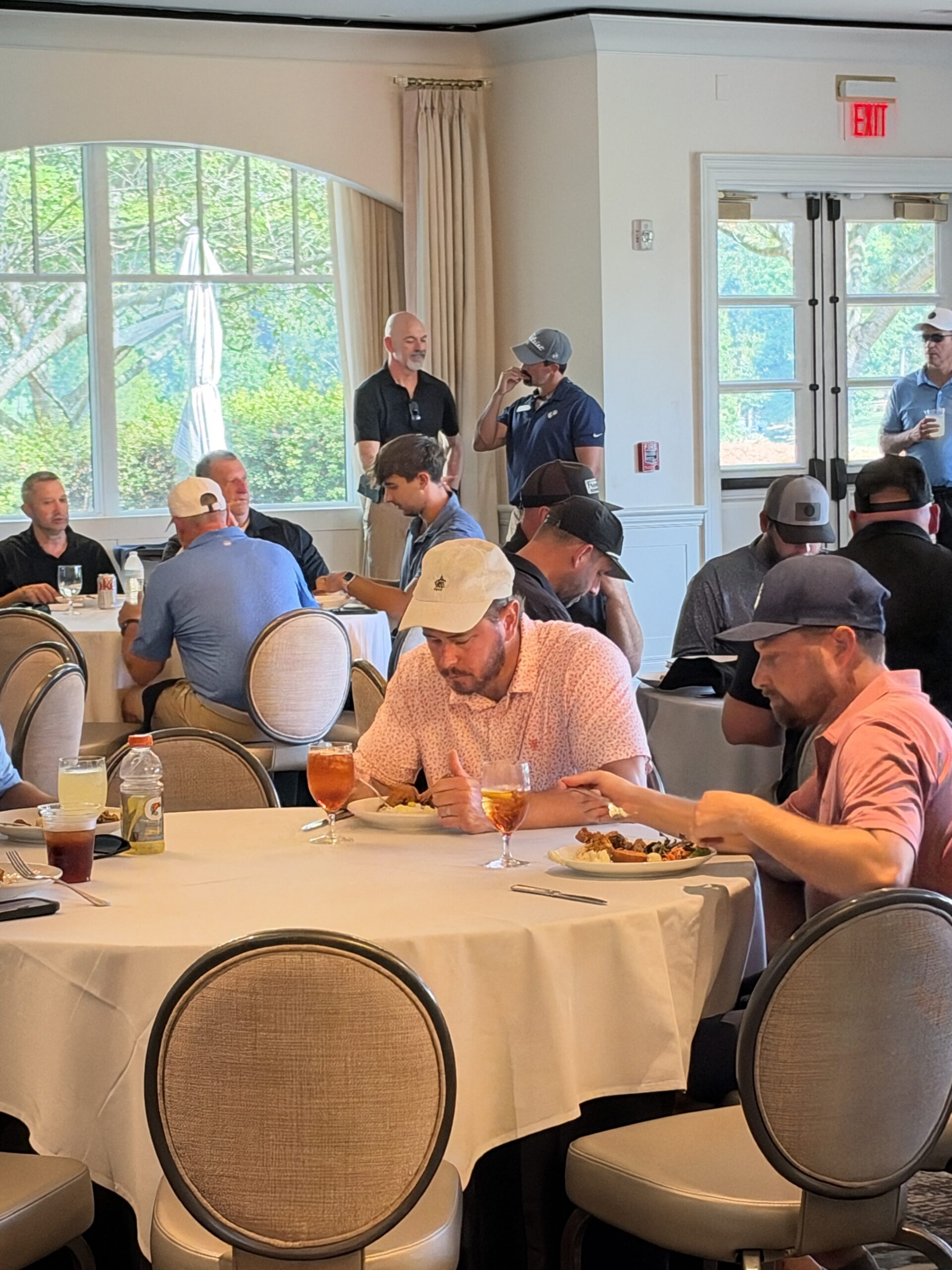 Men in golf attire eat lunch at round tables in a clubhouse dining room during the BCH Golf Classic at Sedgefield Country Club.