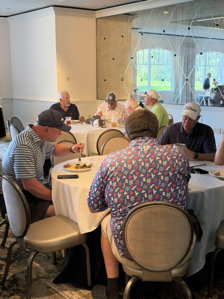 Golfers in polo shirts and caps eat lunch at round tables in a clubhouse dining room during the BCH Golf Classic at Sedgefield.