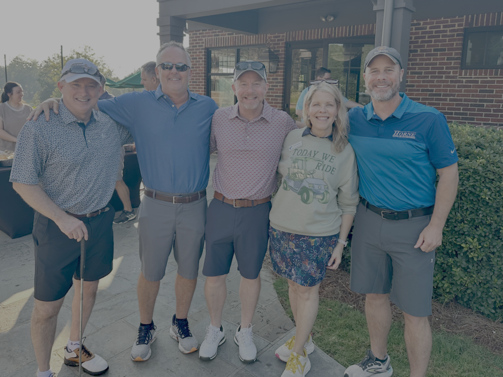 Four men and a woman pose arm in arm outside the clubhouse at the BCH Golf Classic at Sedgefield Country Club.