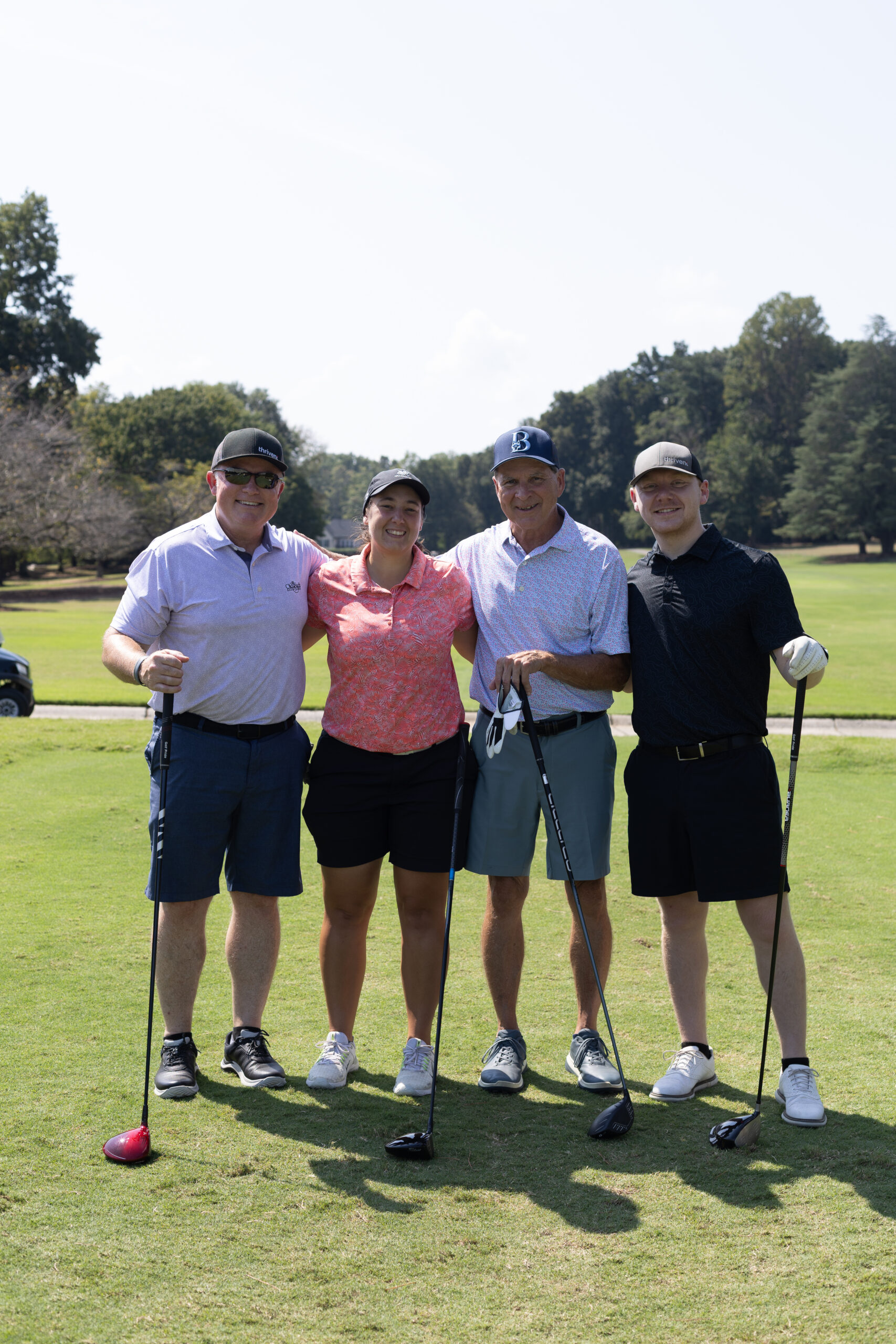 Four golfers with clubs pose arm in arm on the course at the BCH Golf Classic at Sedgefield Country Club.