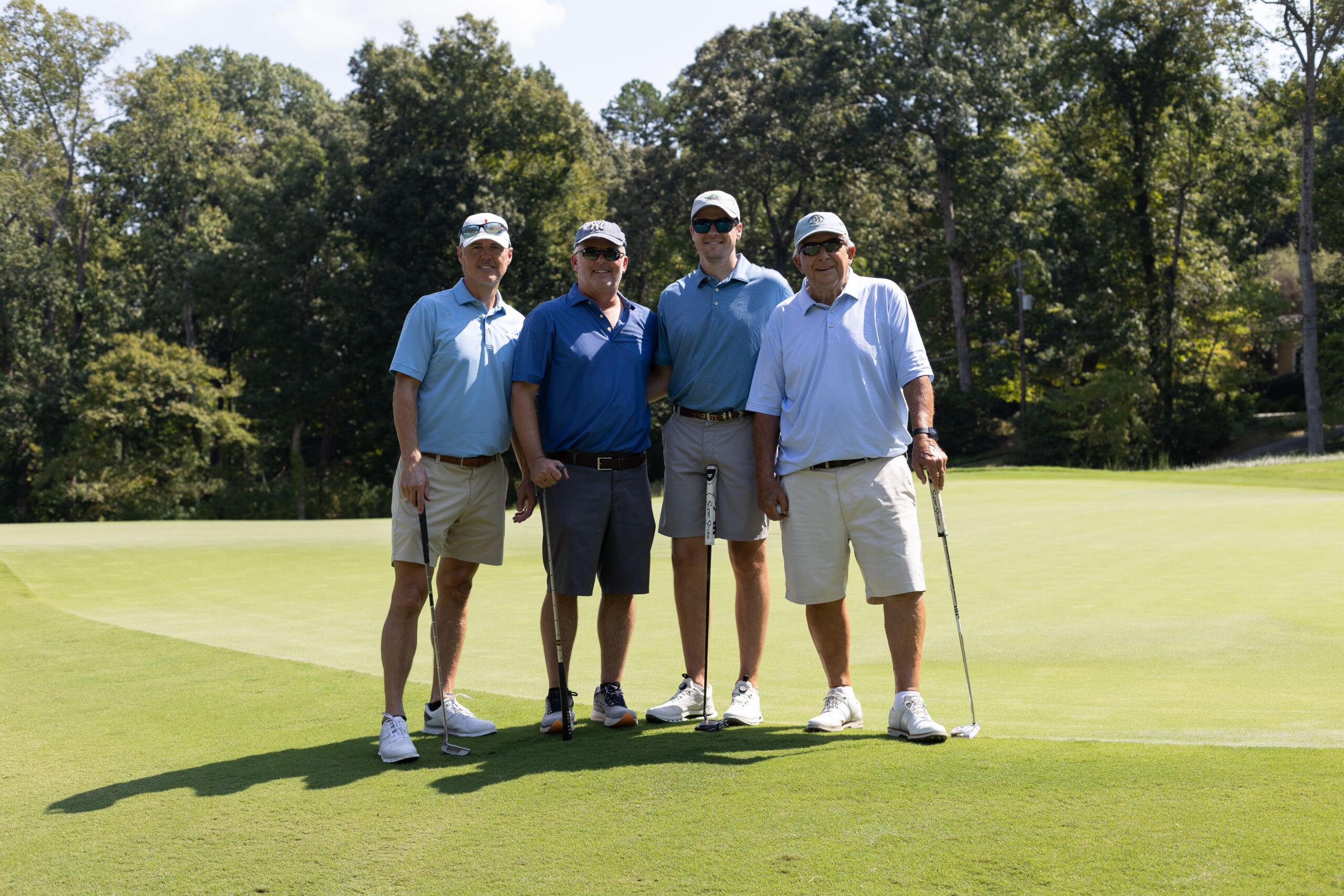Four men in polo shirts and caps pose with golf clubs on a green at the BCH Golf Classic at Sedgefield Country Club.