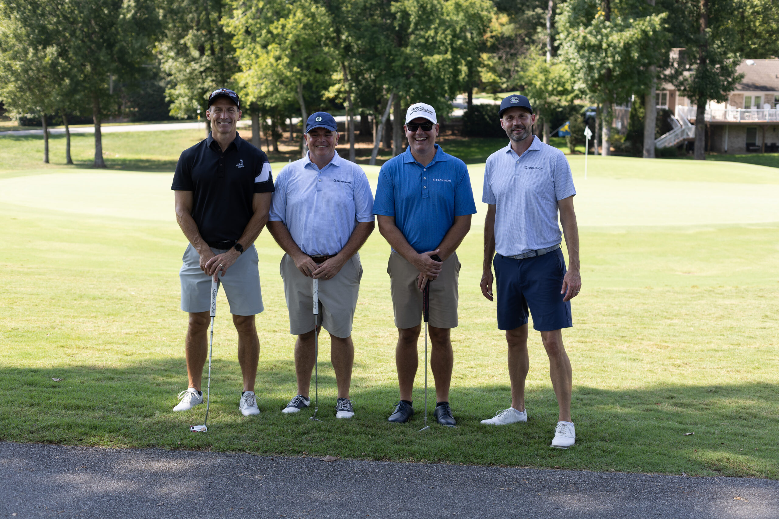 Four men in golf attire pose with clubs on a green at the BCH Golf Classic at Sedgefield Country Club.