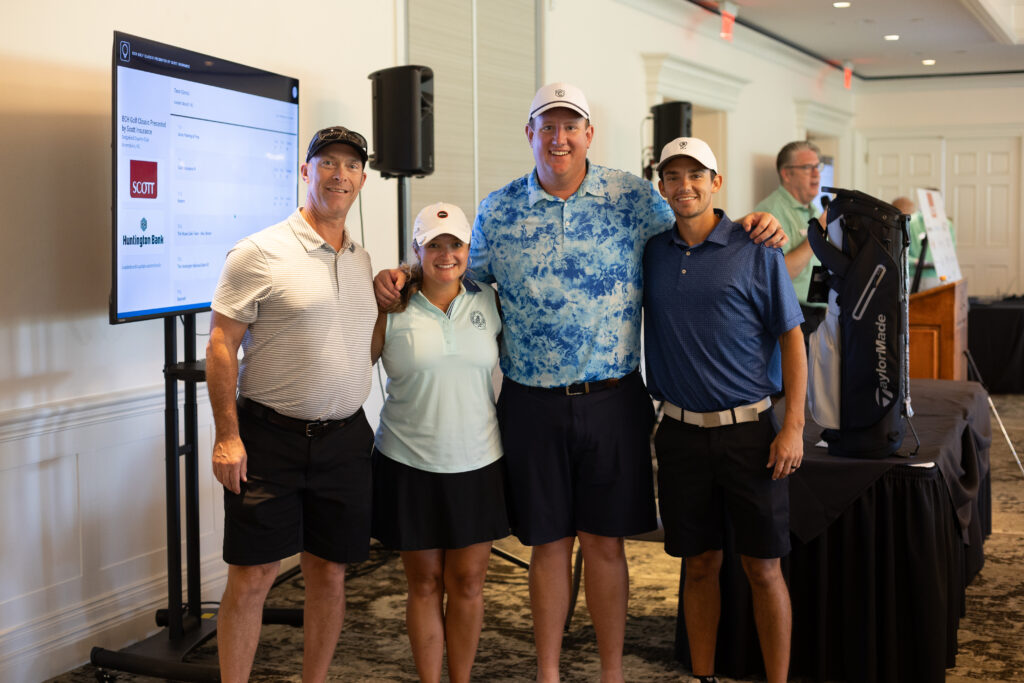 Four smiling golfers pose together indoors at the BCH Golf Classic at Sedgefield Country Club, with sponsor screen behind them.