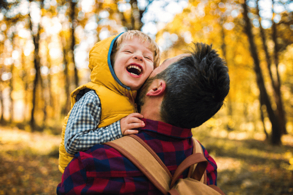 A father hugging his laughing young son outdoors among autumn trees