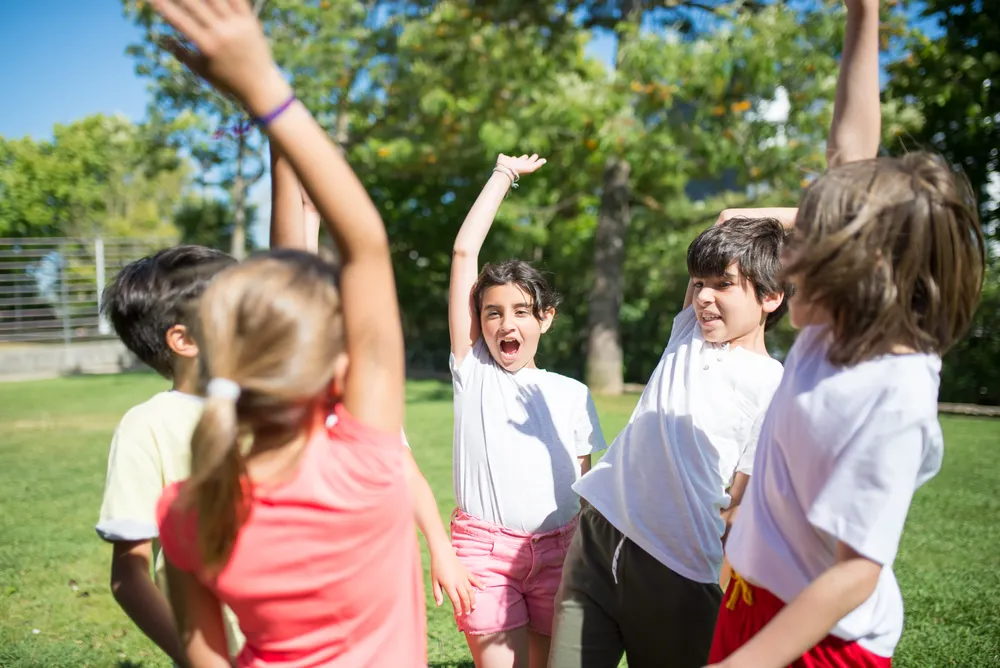 Children cheering with their arms raised while playing in a sunny park