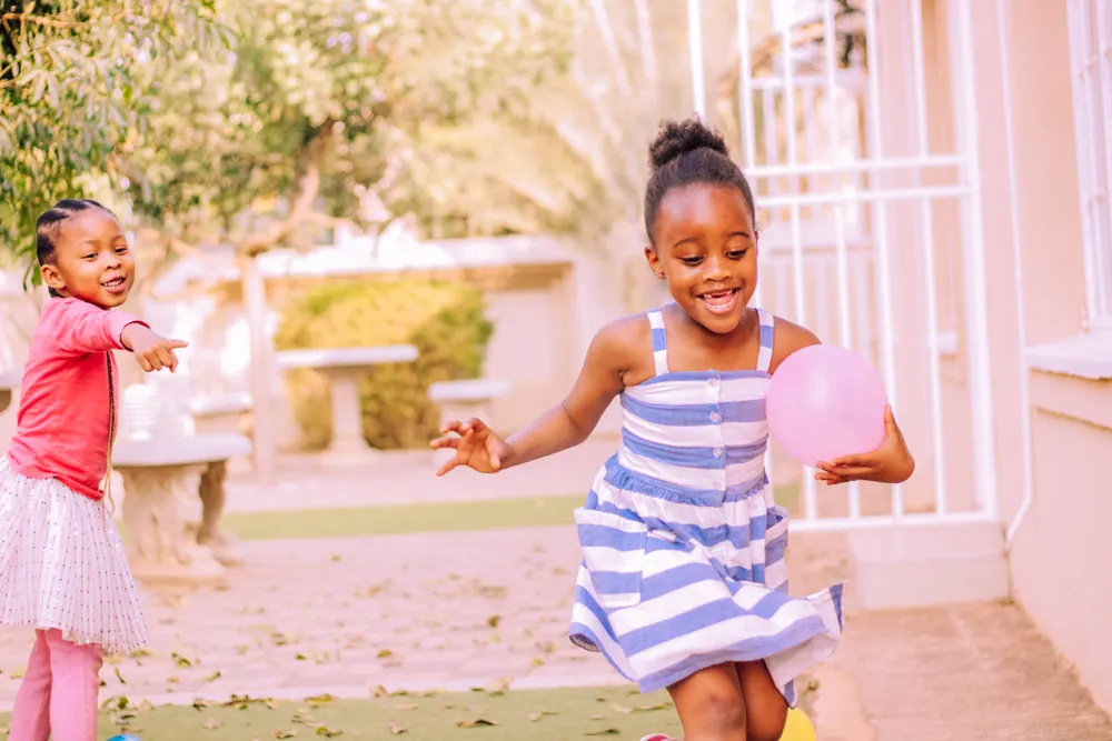 Two joyful little girls playing with balloons outside
