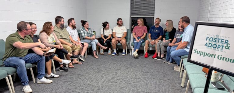 Rich Fork Baptist Church foster care support group members laughing together in a circle beside their support group sign